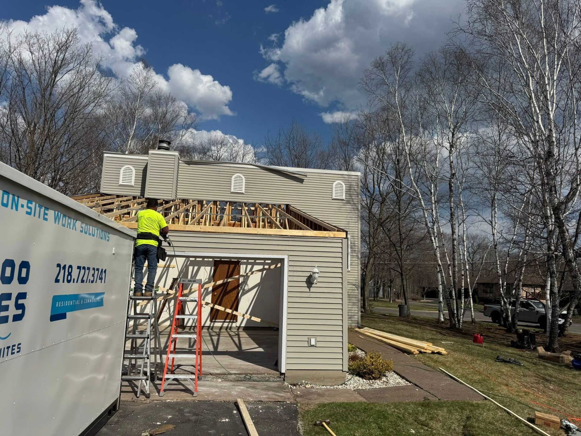 Workers on a ladder installing siding on a small building under a cloudy sky