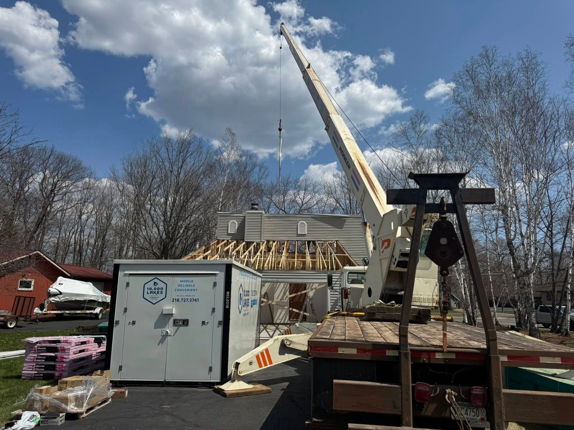 Construction site with a crane, building materials, and a white equipment container under a cloudy blue sky