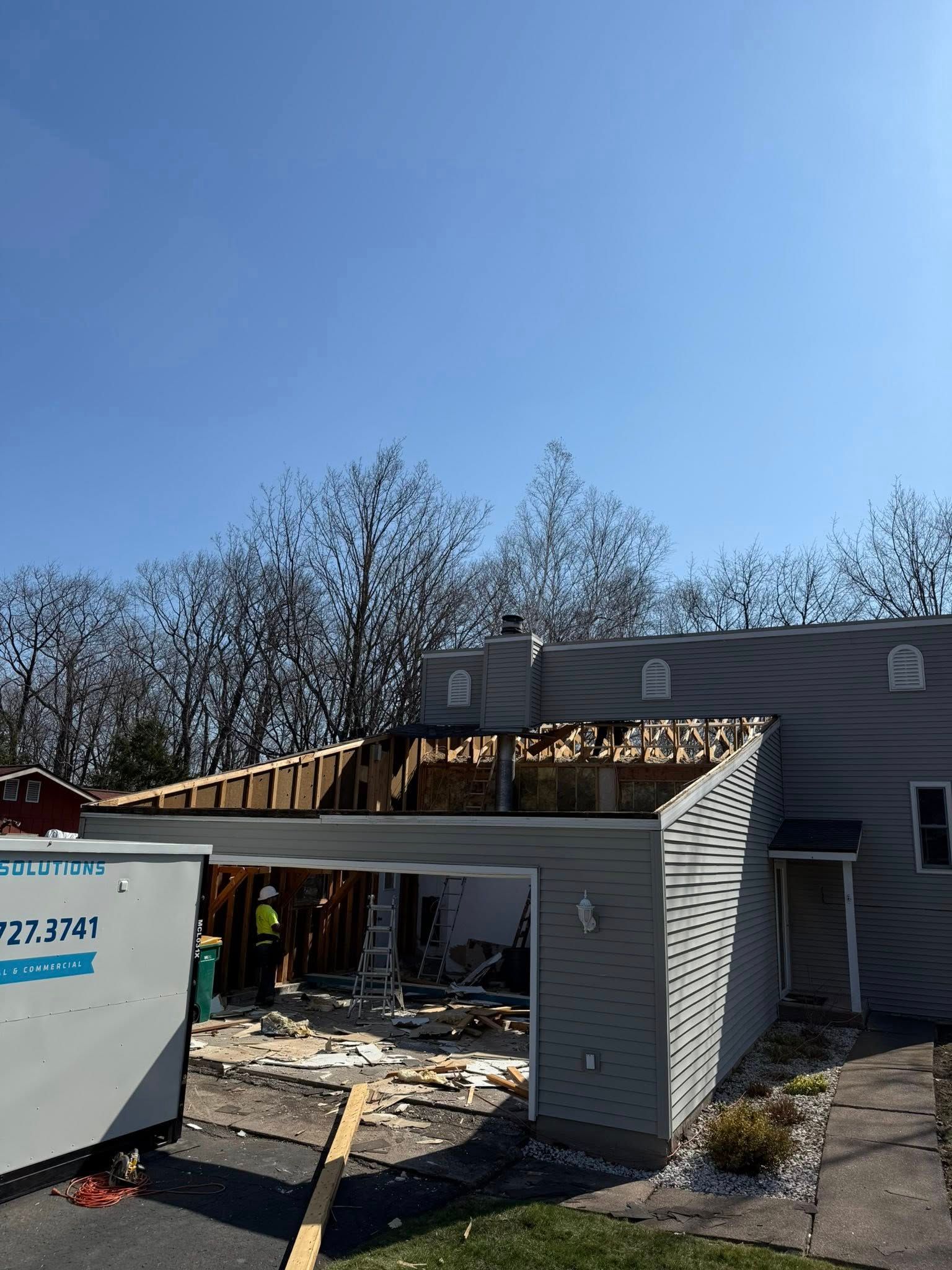 Partially destroyed house with collapsed garage roof and debris under a blue sky