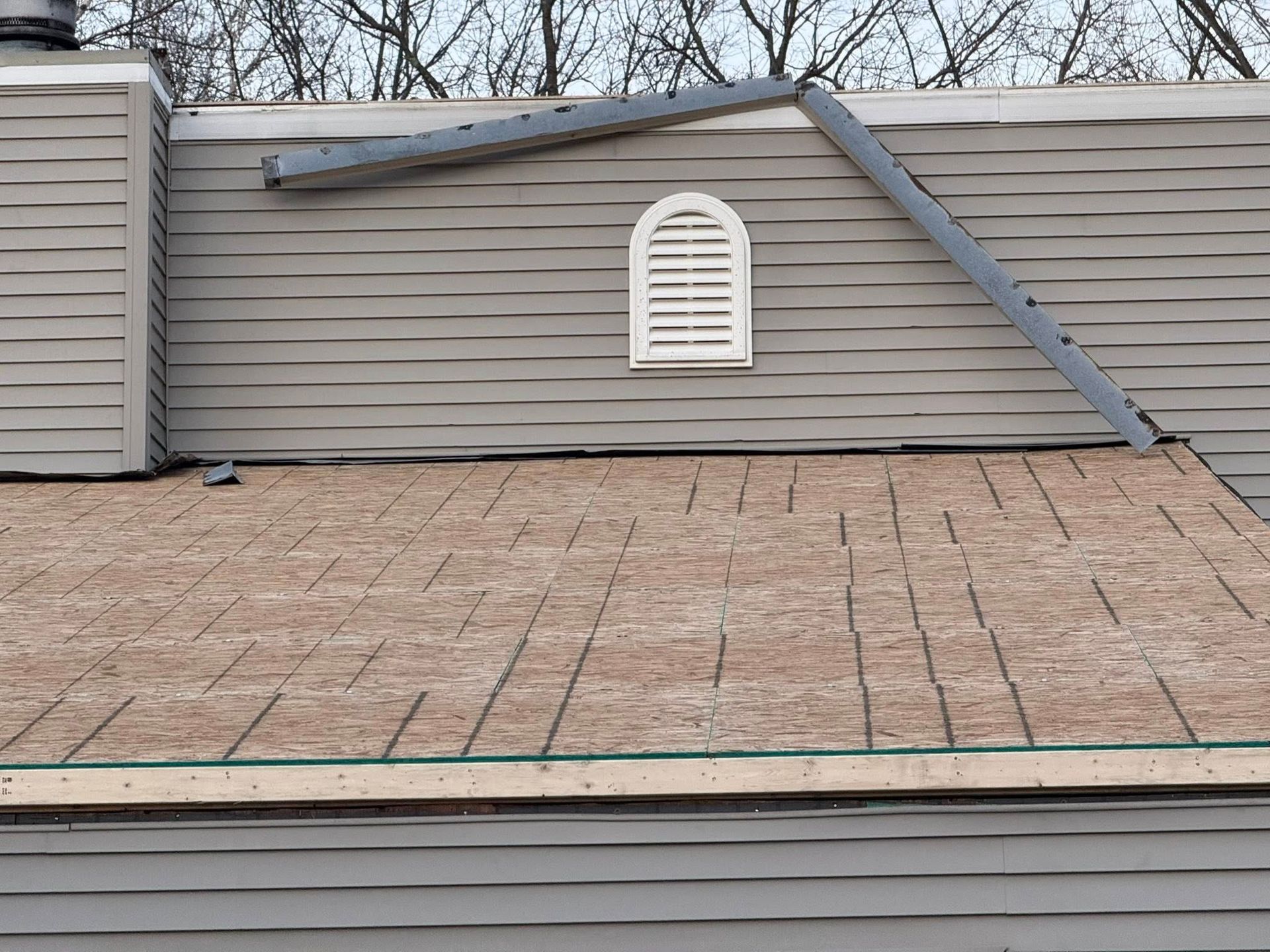 Roof with storm damage, including a bent ridge and a detached dark panel over gray siding.