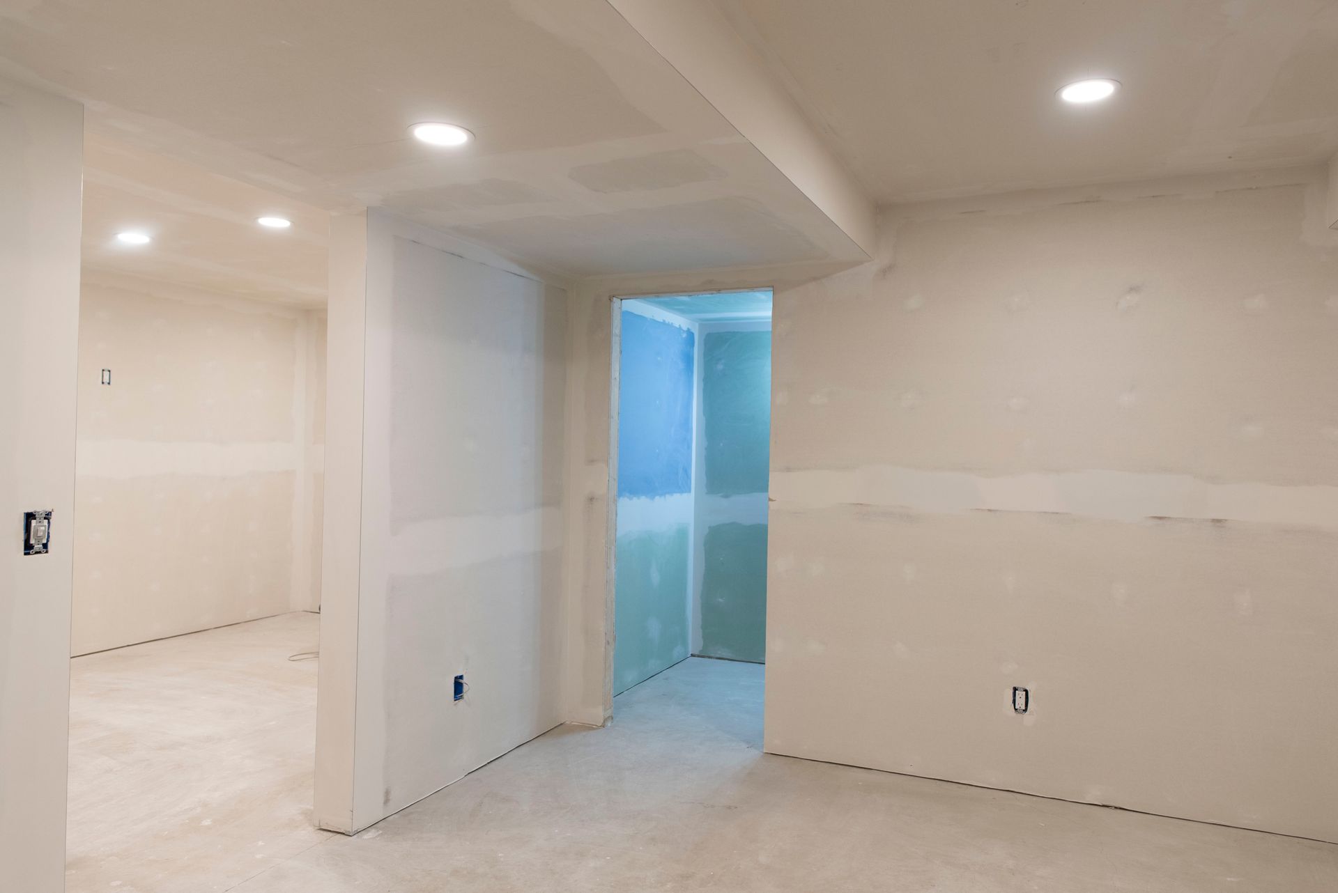 Empty unfinished room with white walls, recessed lights, and a blue-lit doorway under construction