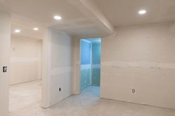 Empty unfinished room with white walls, recessed lights, and a blue-lit doorway under construction