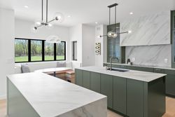 Modern kitchen with white marble counters, green cabinets, black fixtures, and large windows.