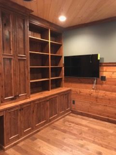 Wood-paneled media room with built-in shelves, cabinets, and a wall-mounted TV