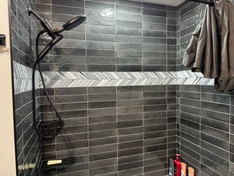 Modern gray-tiled shower with black handheld showerhead, chevron accent strip, and hanging towel