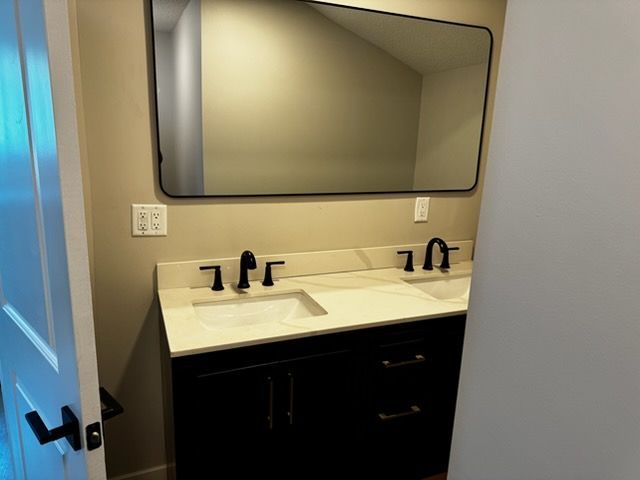 Bathroom vanity with double sink, large mirror, and dark cabinets under warm lighting