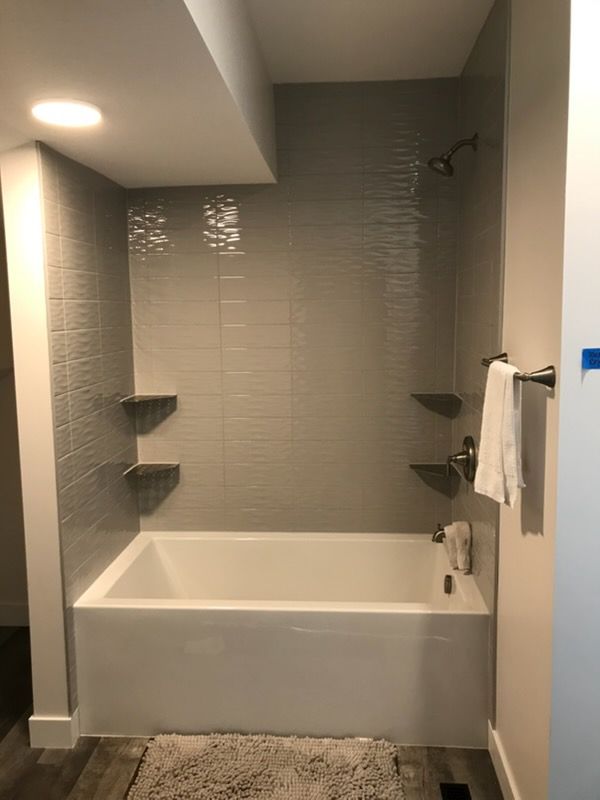 Small modern bathroom with a white tub, gray tiled shower walls, built-in shelves, and a towel rack.