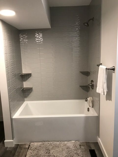 Modern gray-tiled bathroom with a white bathtub, built-in shelves, and a wall-mounted towel rack