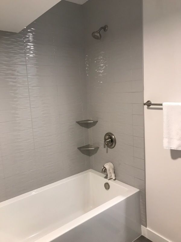 Modern bathroom with white tub, gray tiled walls, shower fixtures, and towel rack