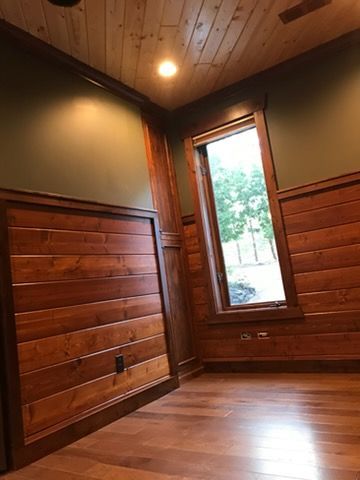 Wood-paneled empty room with a window, hardwood floor, and warm ceiling light