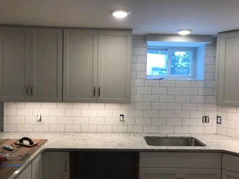 Modern kitchen with gray cabinets, white subway tile backsplash, and a small window above the sink.
