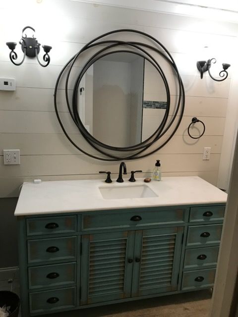 Bathroom vanity with teal cabinet, white countertop, round mirror, and black wall sconces.