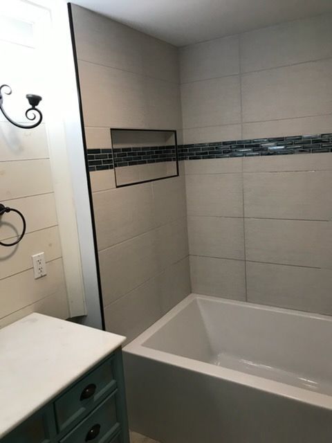Modern bathroom with white tub, tiled shower walls, and a teal vanity edge