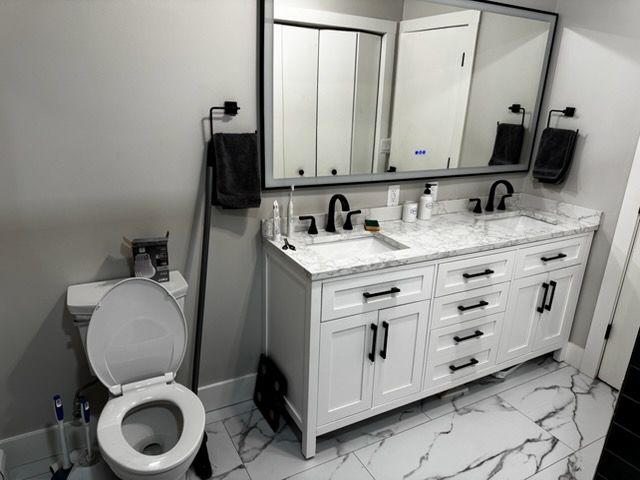 Modern bathroom with white vanity, double mirrors, black fixtures, and toilet on the left.