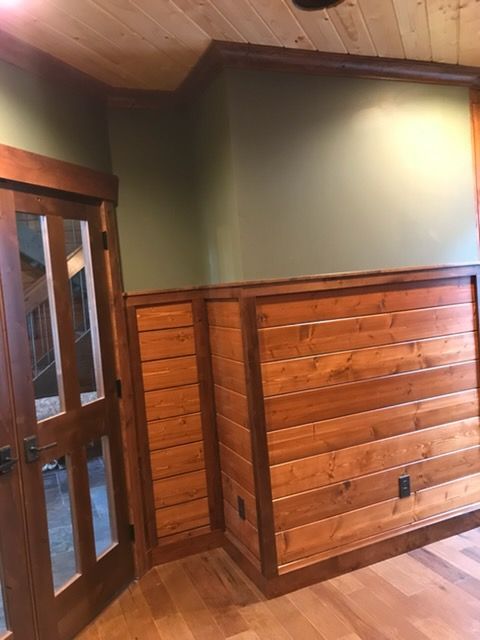 Wood-paneled room corner with green walls, wooden floor, and glass-paneled doors on the left.