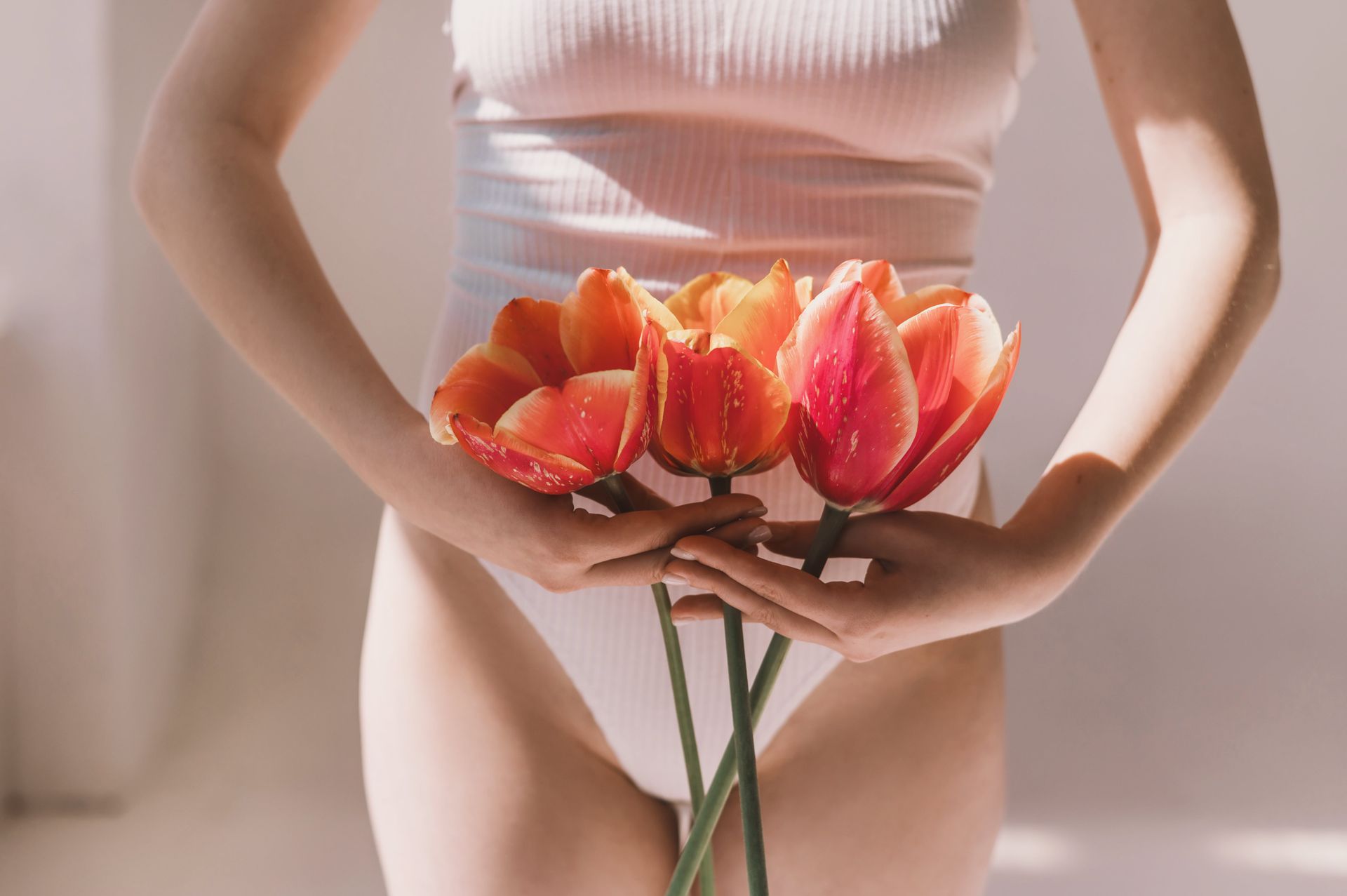 Uma mulher de calcinha está segurando flores na frente do estômago.