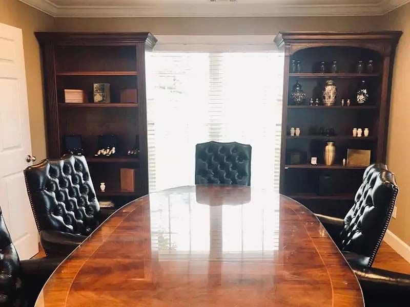 Wooden office with a large desk, leather chairs, and bookshelves flanking a bright window.