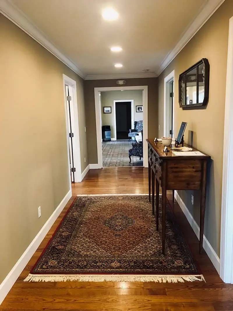 Hallway with hardwood floor, rug, small table, mirror, and doorways.
