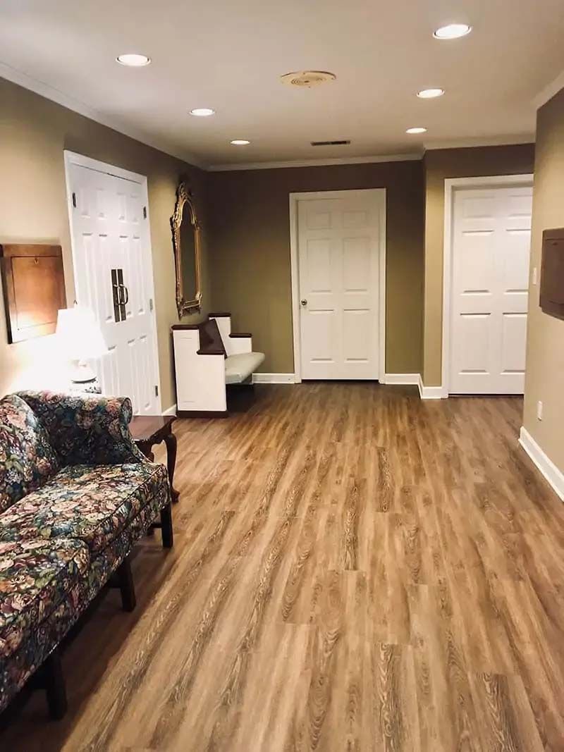 A room with wood-look flooring, couch, white doors, and a bench. The walls are tan.