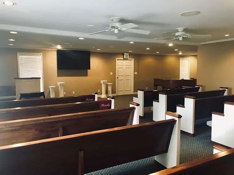 Interior of a chapel with pews, ceiling fans, and a door at the end.