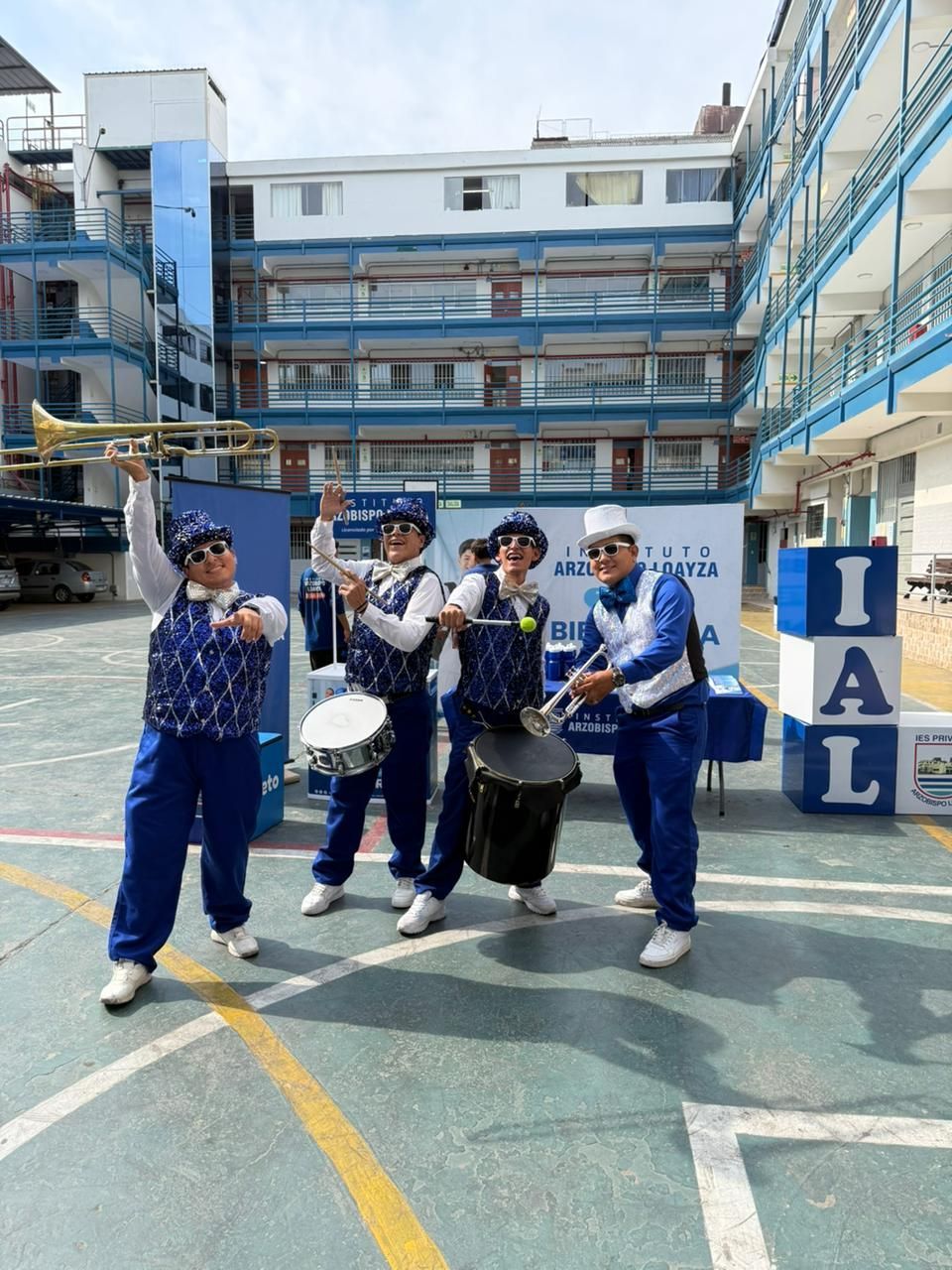 Cuatro músicos con uniformes azules y blancos idénticos posan con sus instrumentos en el patio de una escuela