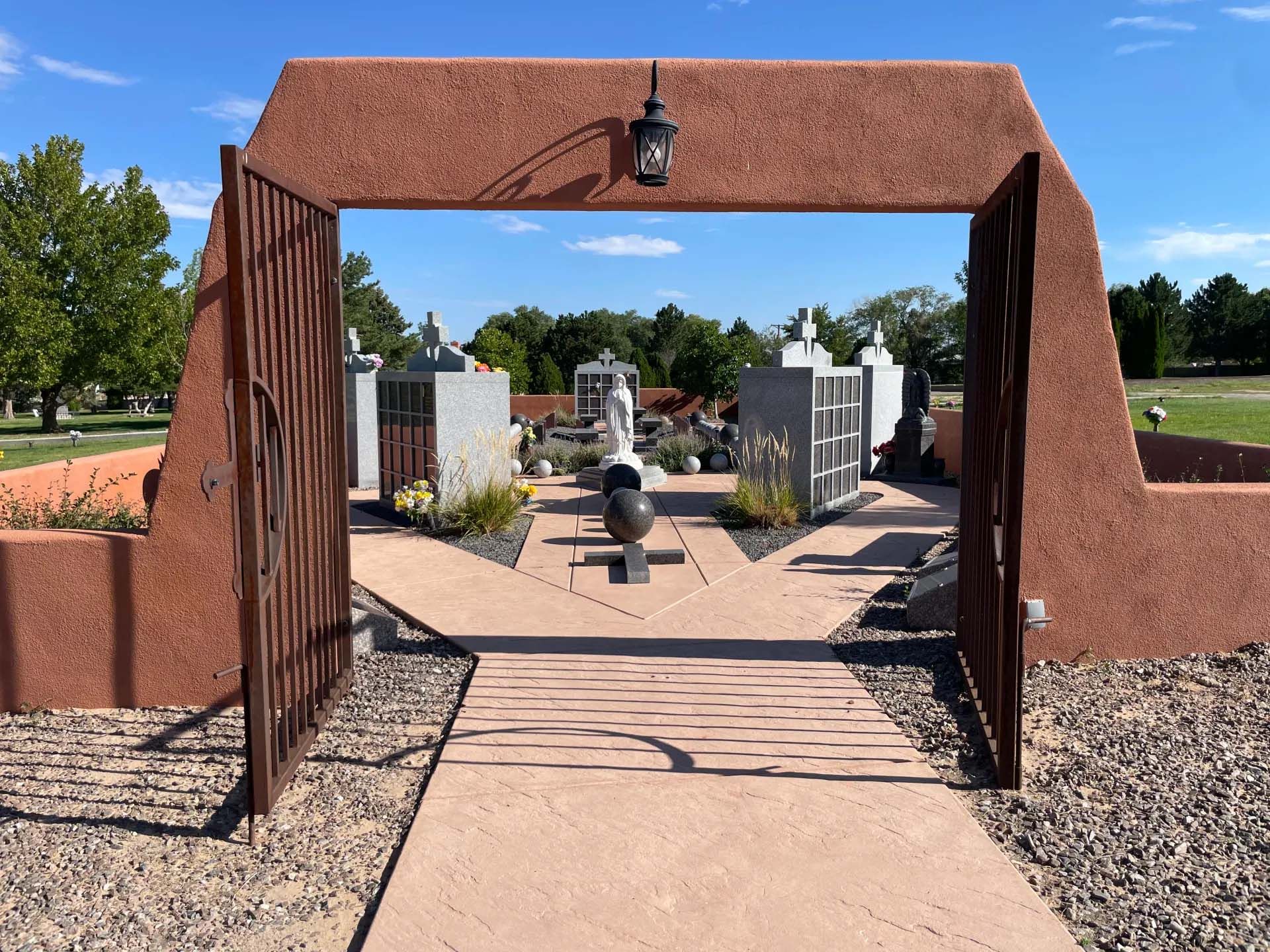 Entry gate of a cemetery with red walls and metal gate; several headstones in the background.
