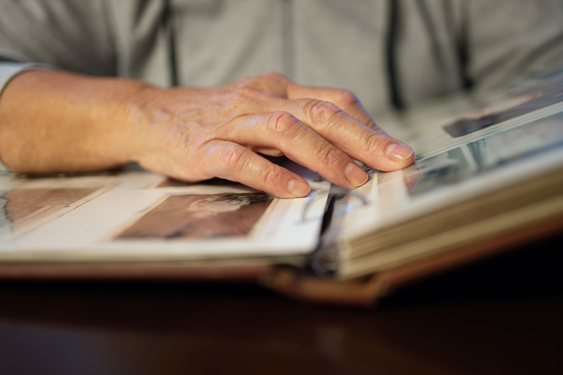 Hand on an open photo album, touching a photograph. Brown album, photos with various contents.