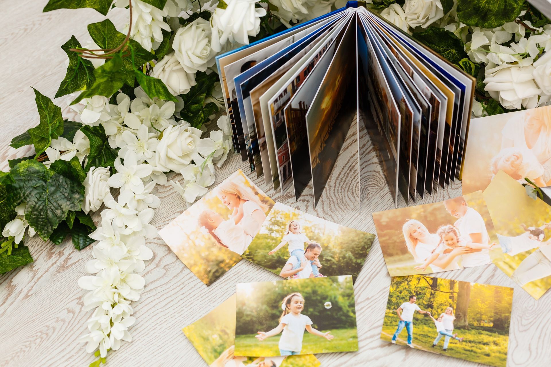Photo album open, surrounded by loose photos and white flowers on a light-colored surface.