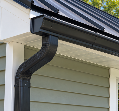 Rain gutter on a gray shingled roof above green grass