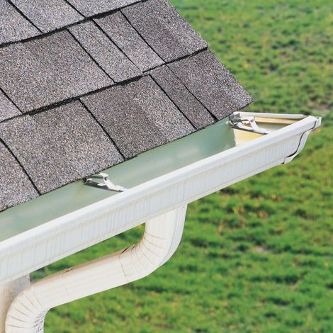 Rain gutter on a gray shingled roof above green grass