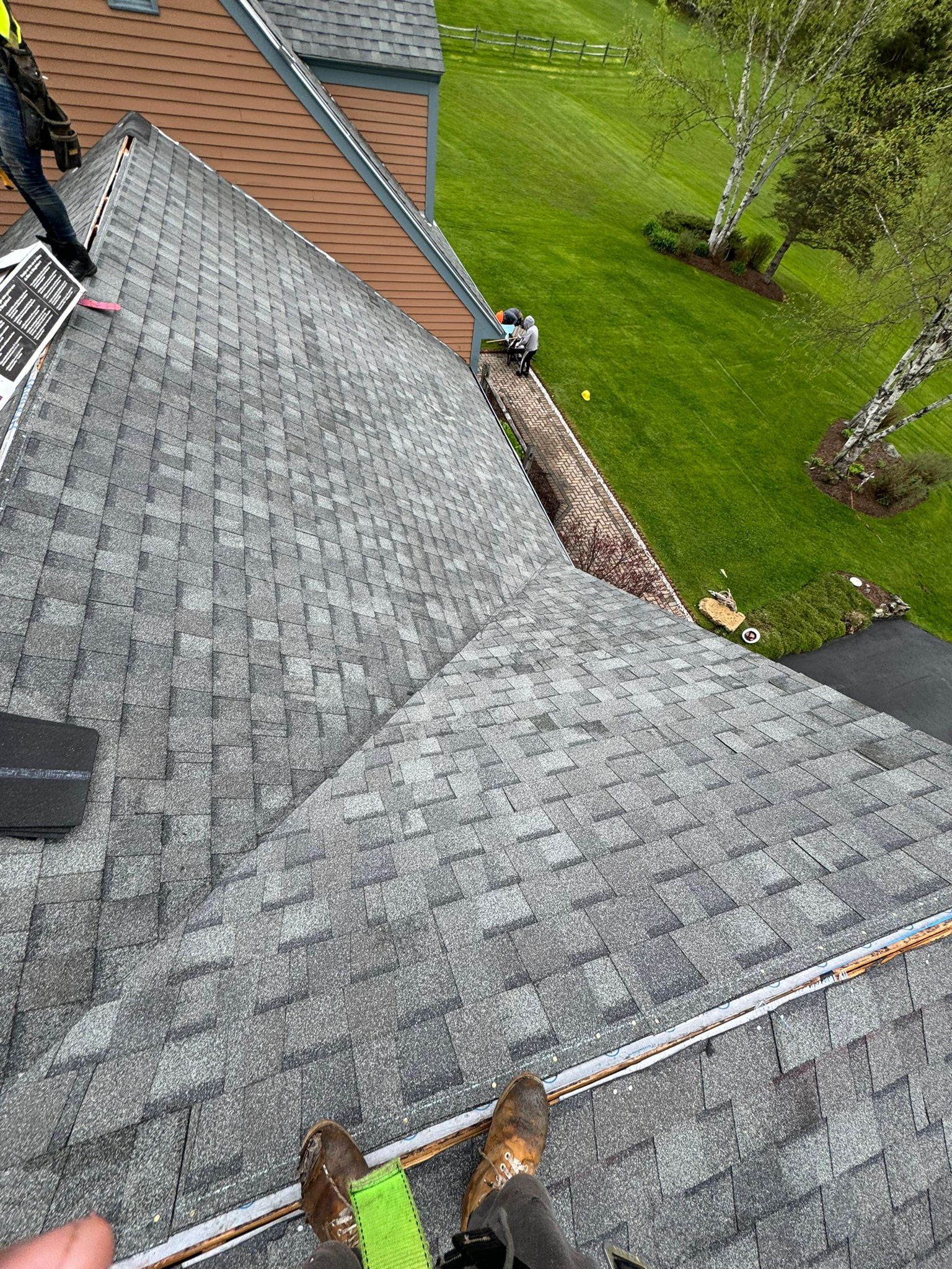 View from a roof with gray shingles overlooking a green yard and a house below