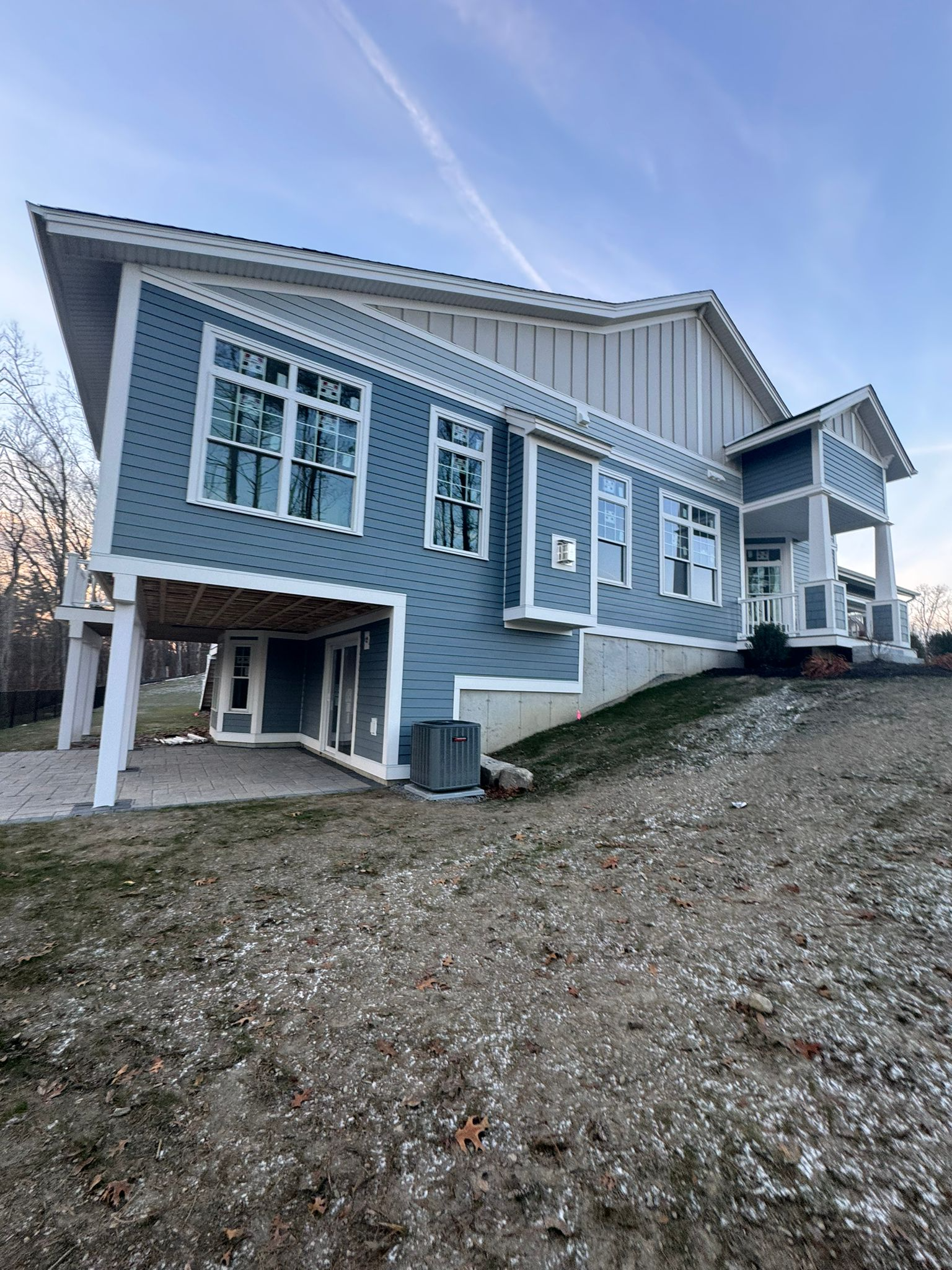 Blue house on a snowy hillside with white trim and a sloped driveway