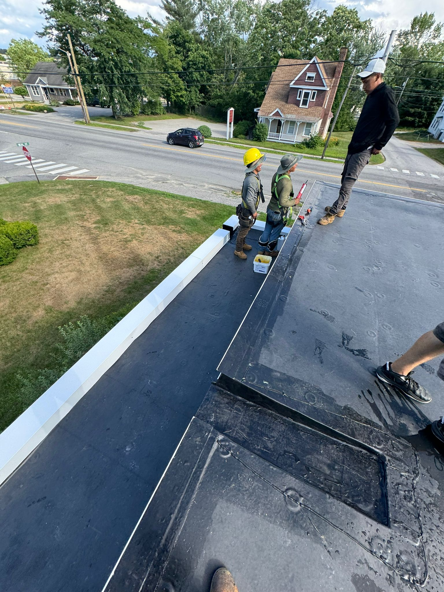 Workers repainting a curb and sidewalk edge beside a street and grassy lawn