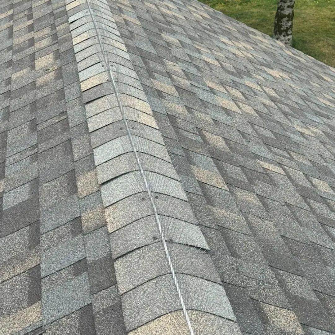 Close-up of a gray shingled roof with a ridge line and roof vent flashing