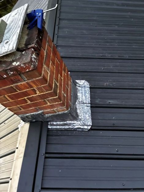 Close-up of a brick chimney flashing repaired with silver sealant against dark metal siding.