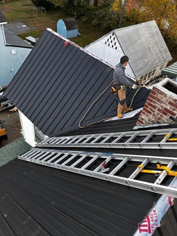 high shot of worker standing on standing seam metal roof replacement project. Black metal roof.