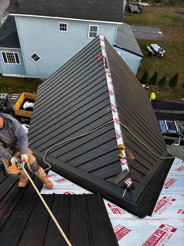 Roofing workers installing a dark metal roof on a house