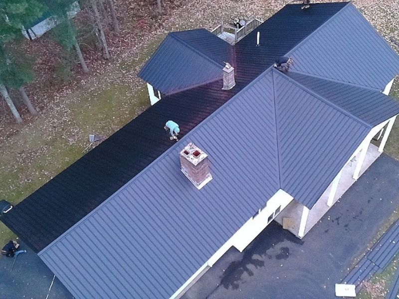 Aerial view of a gray-roofed house with two people on the roof and a black driveway below.