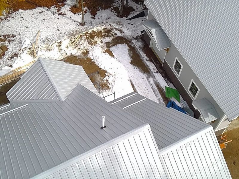 Snow-covered metal rooftops beside a house and yard seen from above.