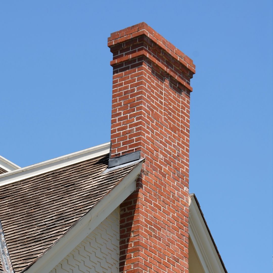 Brick chimney rising above a house roof against a clear blue sky