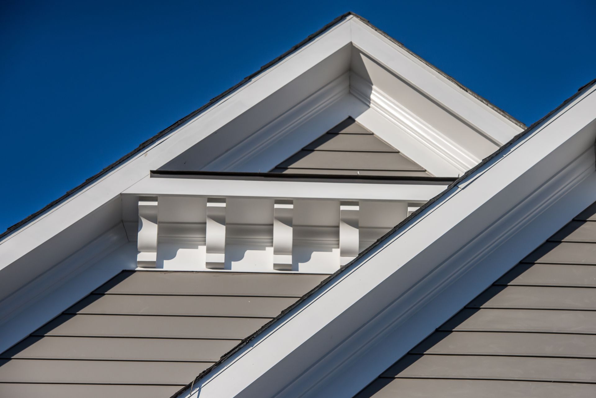 White house gable with decorative trim and beige siding against a bright blue sky