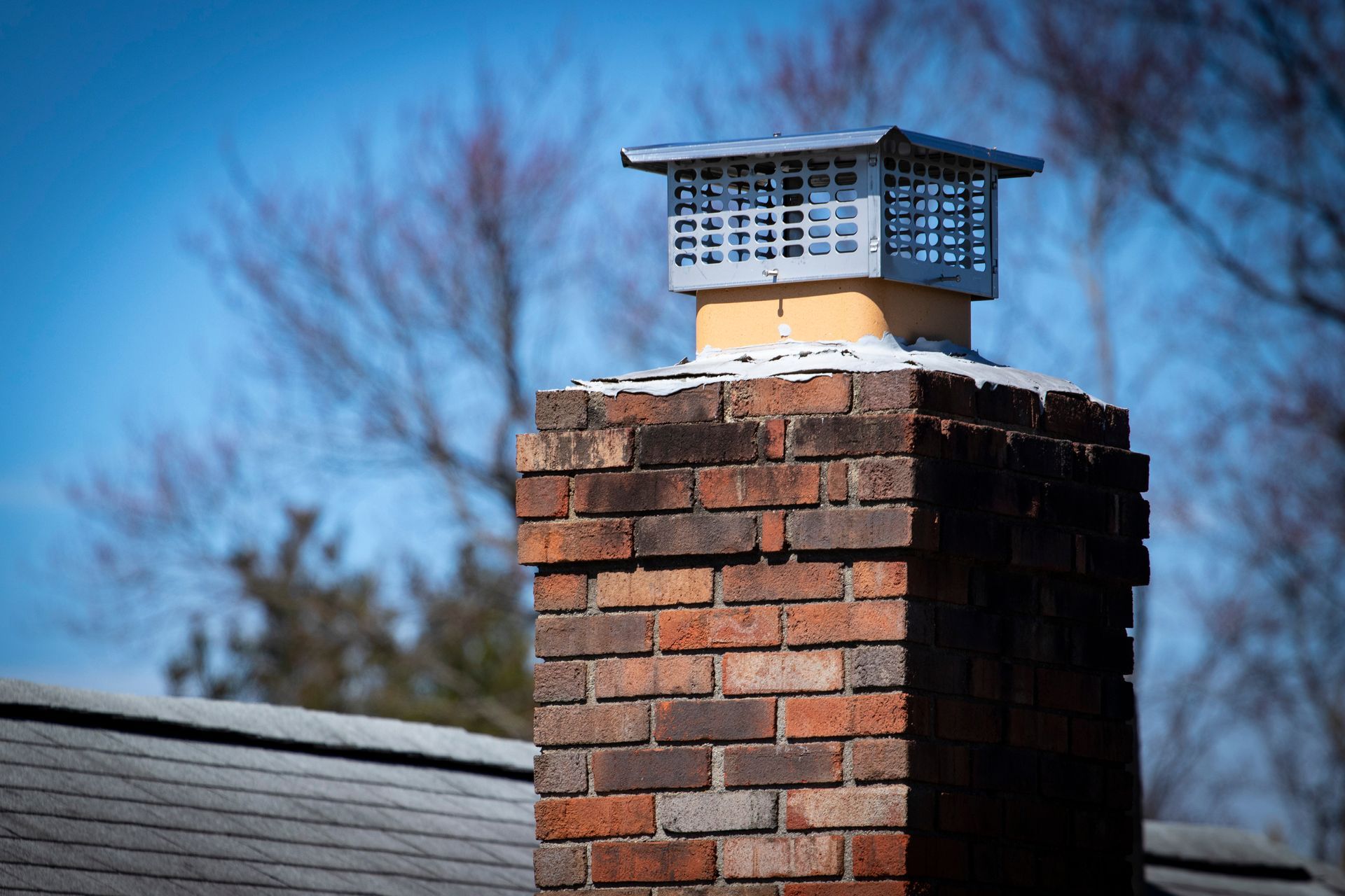 Brick chimney with a metal cap against a blue sky