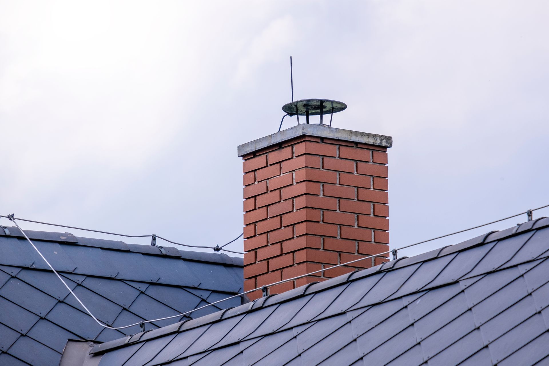 Brick chimney on a gray metal roof against a cloudy sky