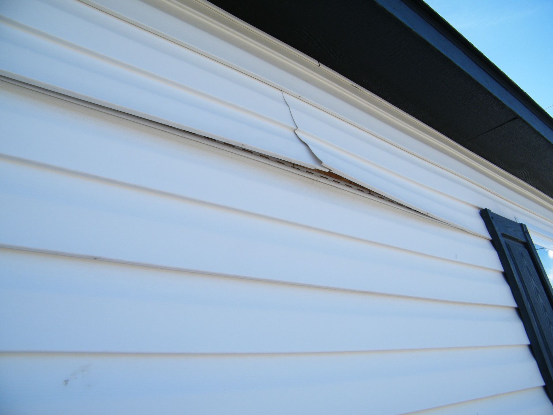 White vinyl house siding with a crack near the roofline and a dark gutter at the top right