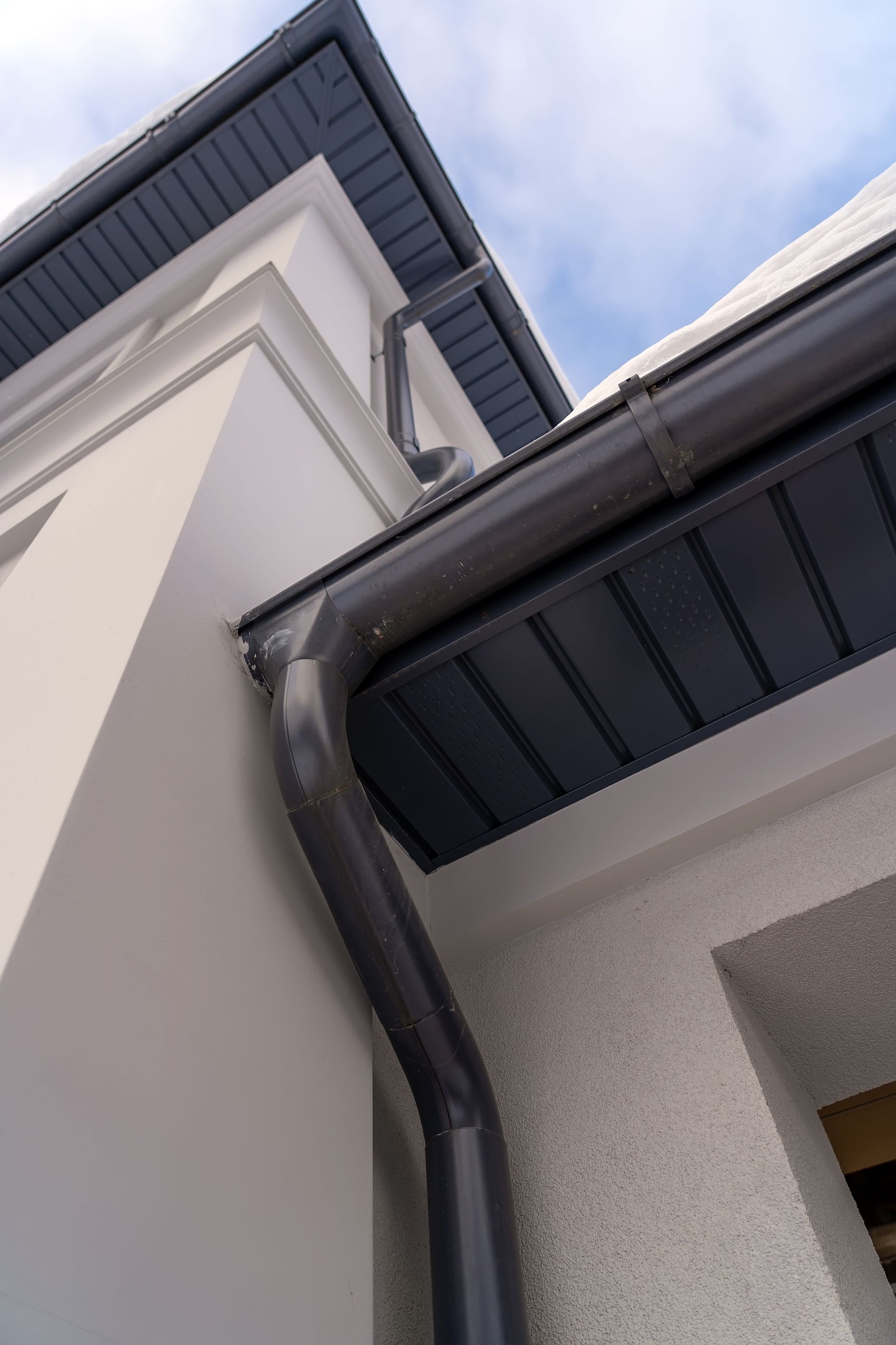 Close-up of a white house exterior with dark gray gutters and eaves against a cloudy sky