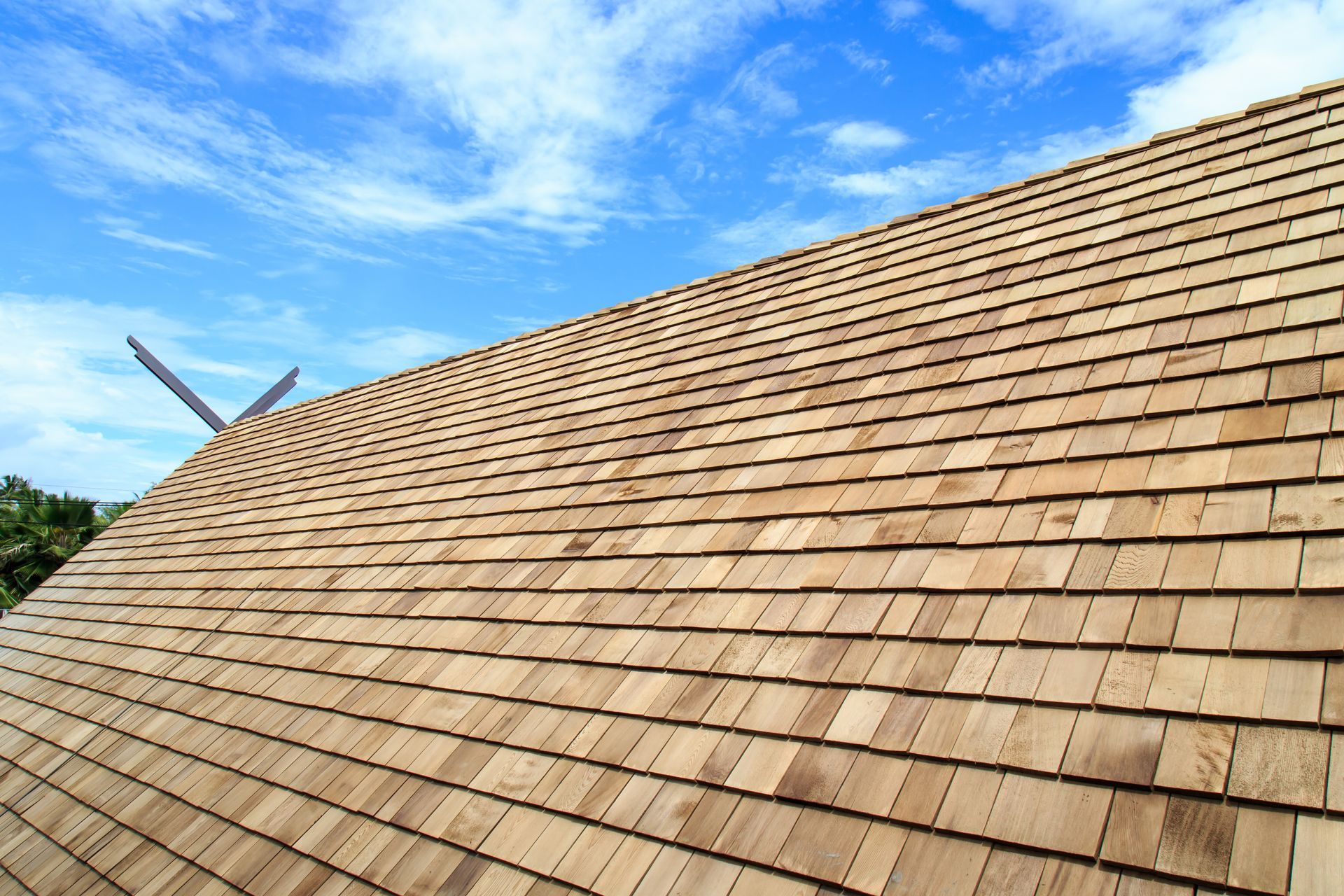 Wooden shingle roof under a bright blue sky with scattered clouds
