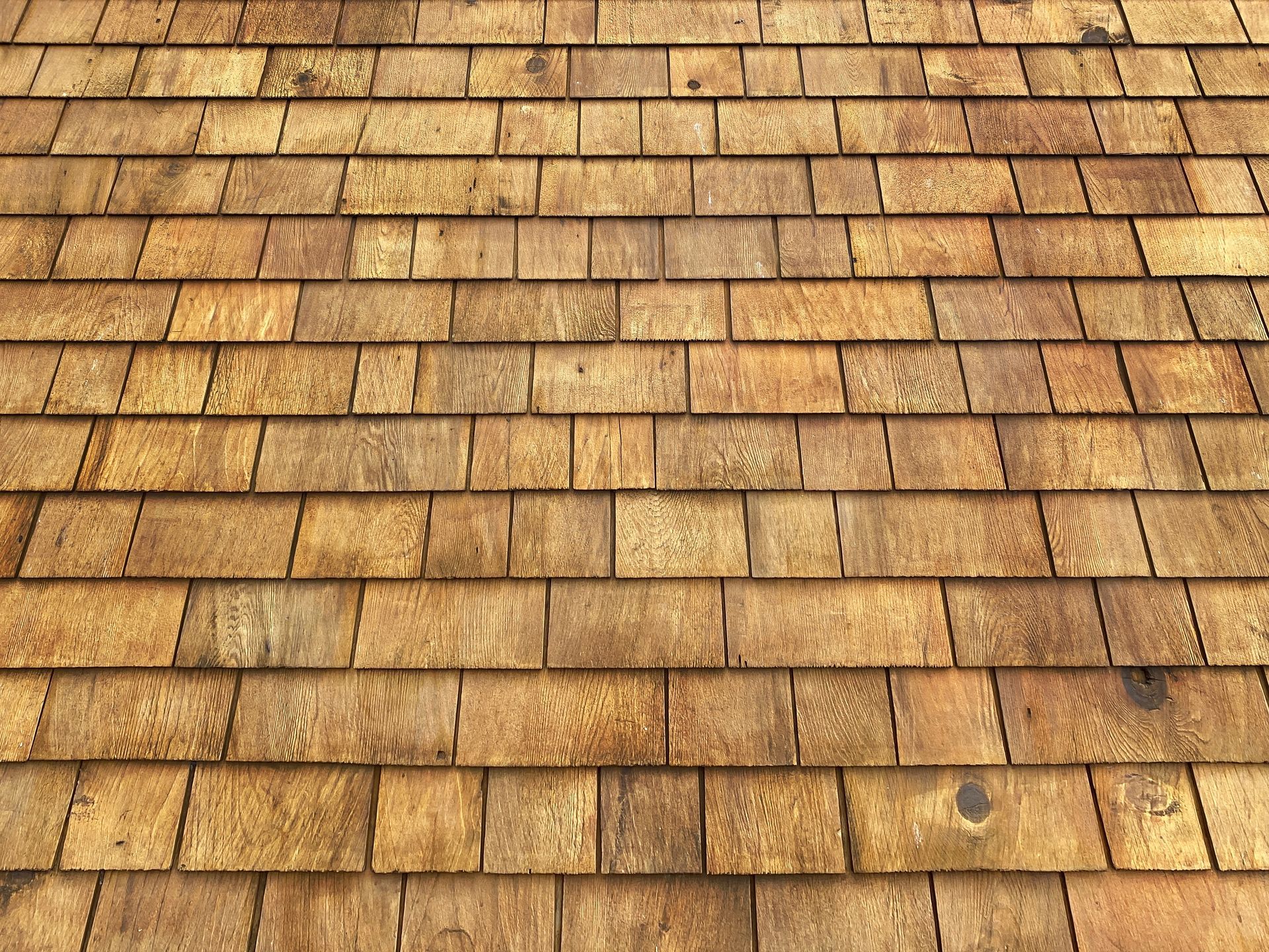 Close-up of a weathered tan wooden shingle roof with rows of overlapping shingles