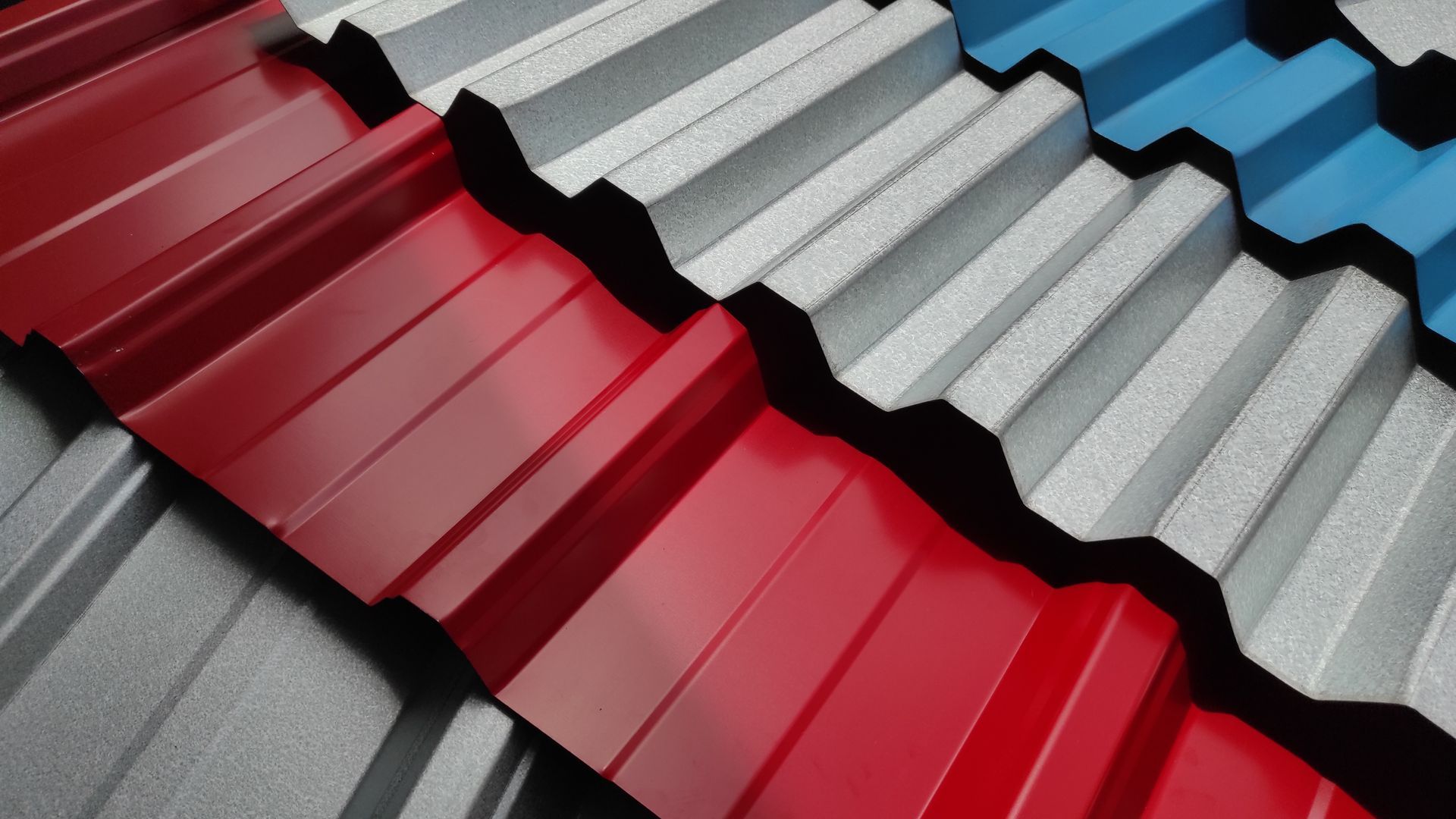 Stacked corrugated metal roofing panels in red, gray, and blue, arranged diagonally