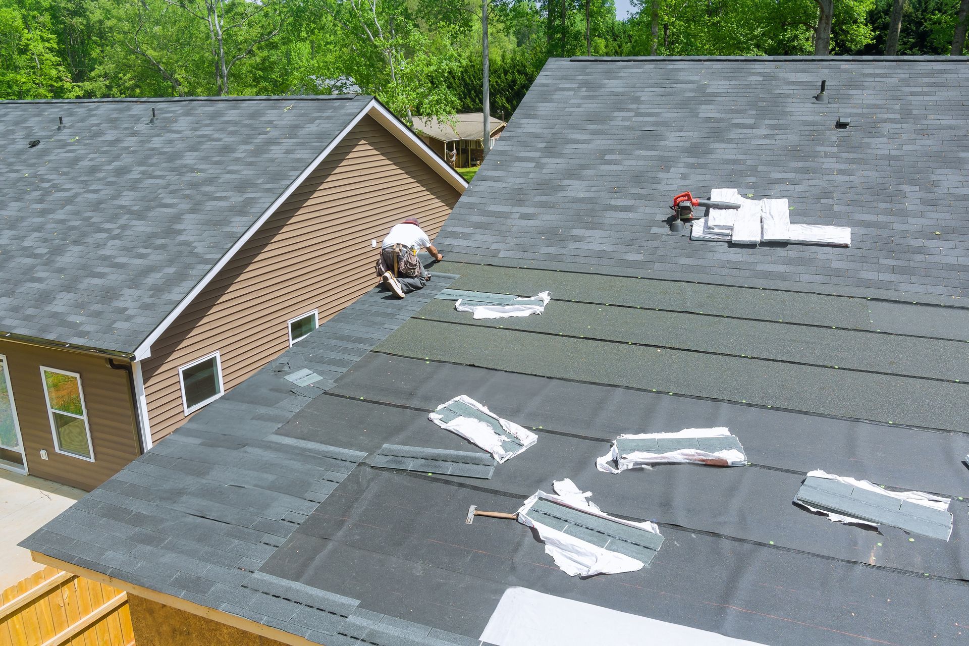 Roofers repairing a dark gray shingle roof on a brick house with scattered materials and tools