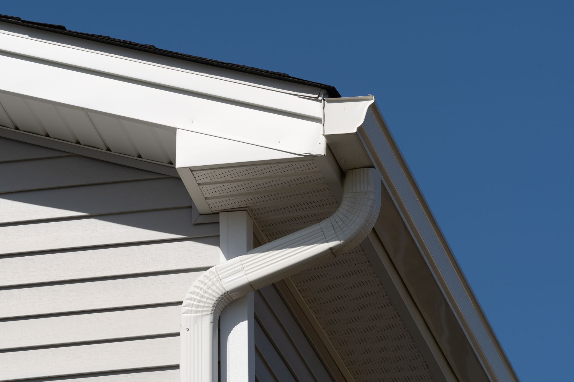 White house gutter and downspout at the roof corner against a blue sky